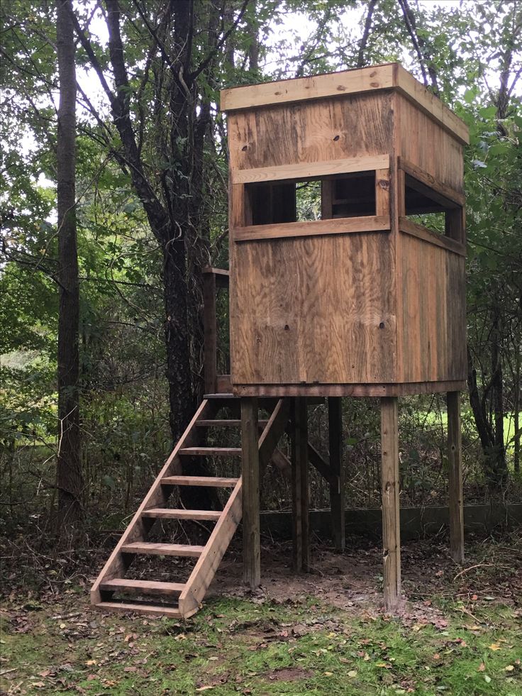 a wooden tree house with stairs in the woods next to it and trees behind it