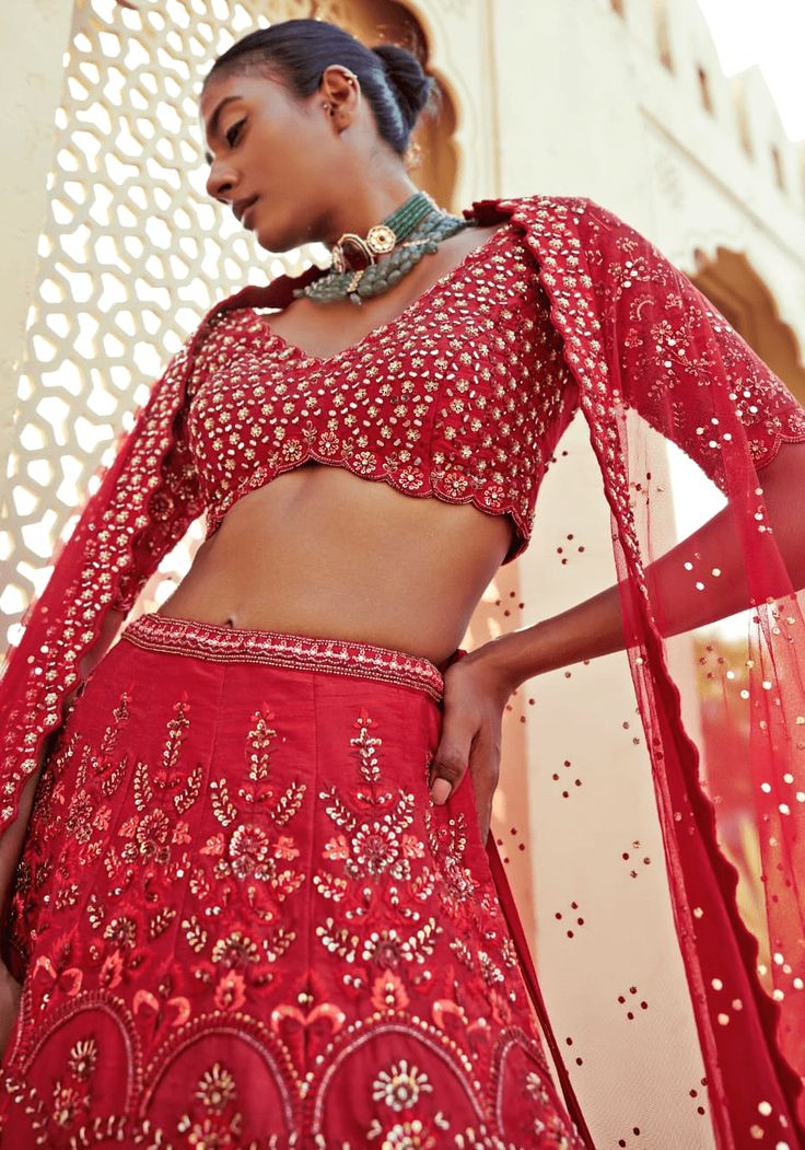 Embrace the epitome of bridal magnificence with our Royal Red Silk Lehenga Set! Designed for the bride who seeks to dazzle, this red bridal lehenga boasts sumptuous raw silk illuminated by floral embroidery, delicate thread work, and shimmering sequin details. The scallop-edged V-neck blouse, with elbow-length sleeves, is heavily embroidered, offering a regal silhouette. Completing the ensemble is a soft net dupatta with an embroidered border and enchanting badla work that cascades gracefully, perfect for your wedding day statement. Make your walk down the aisle unforgettable in this heirloom-quality masterpiece. Composition : Lehenga, Blouse, Dupatta - Raw Silk, Soft Net Care: Dry Clean Only and Vacuum Storage This product can be customized for sleeves, length of blouse and neckline Deliv Red Silk Lehenga, Badla Work, Red Bridal Lehenga, Bridal Lehenga Red, Vacuum Storage, Indian Wedding Wear, Lehenga Blouse, Embroidered Border, Silk Lehenga