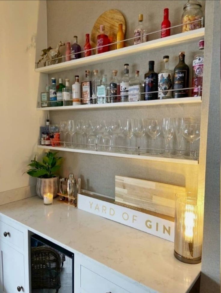 a shelf filled with lots of bottles and glasses on top of a white countertop