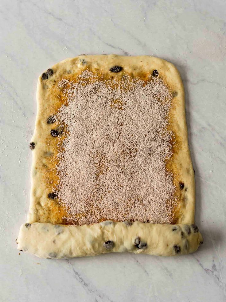 an uncooked pastry sitting on top of a counter with powdered sugar and raisins