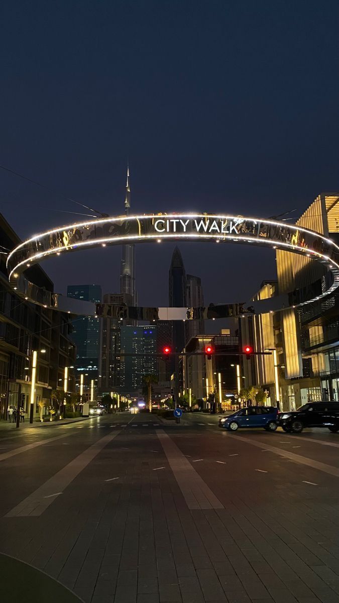 an empty city street at night with cars driving under the bridge that reads city walk