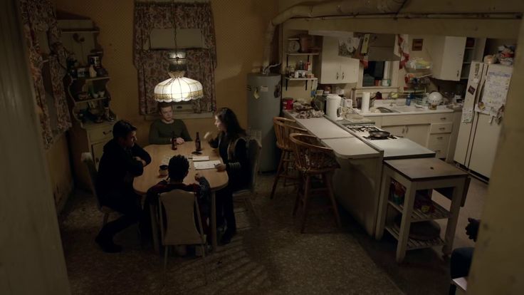 three people sitting at a table in a small room with an open kitchen and dining area