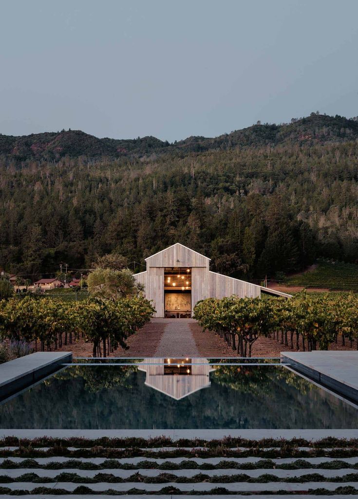 an outdoor pool surrounded by trees and bushes with a barn in the background at dusk