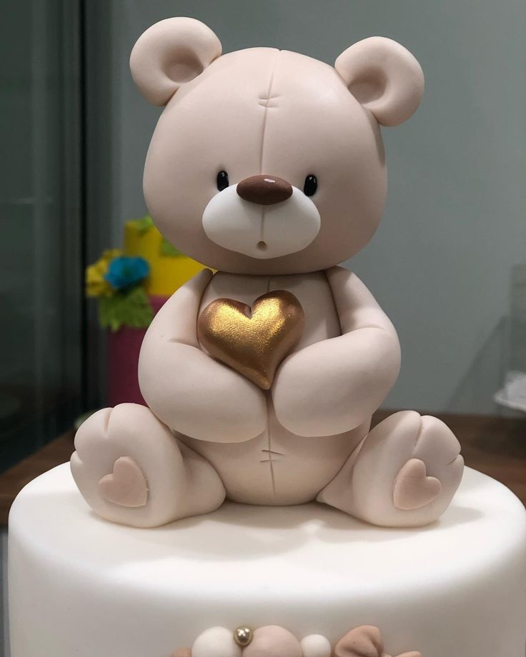 a white cake with a teddy bear holding a gold heart on it's top