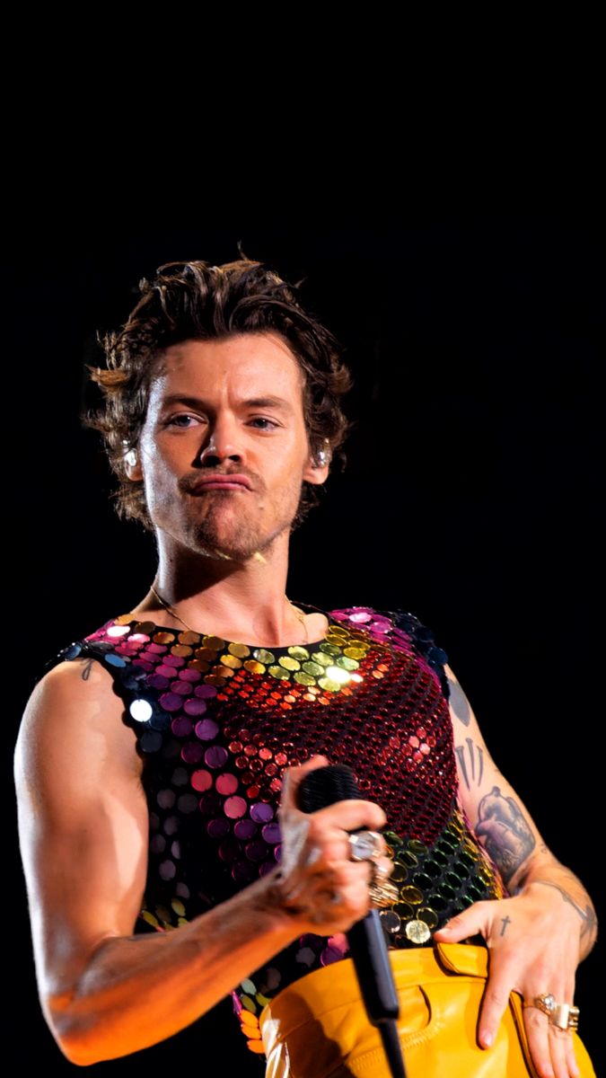 a man holding a microphone in his right hand and wearing a colorful shirt on stage