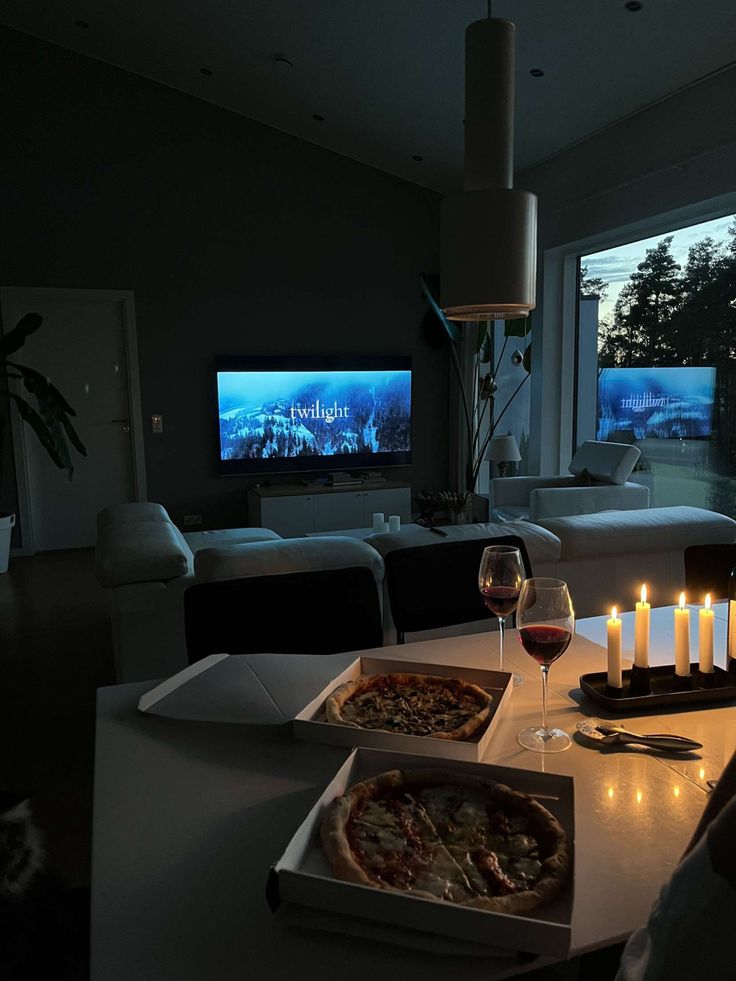 two pizzas on a table with candles in front of a tv and some wine glasses