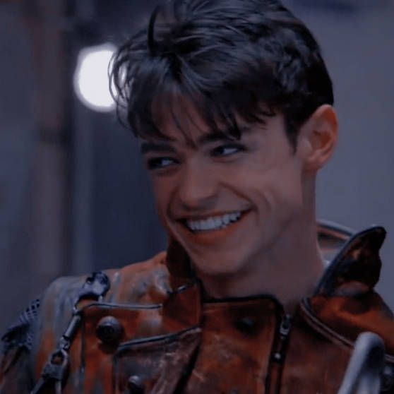 a smiling man in an orange leather jacket with metal accents on his chest and shoulder