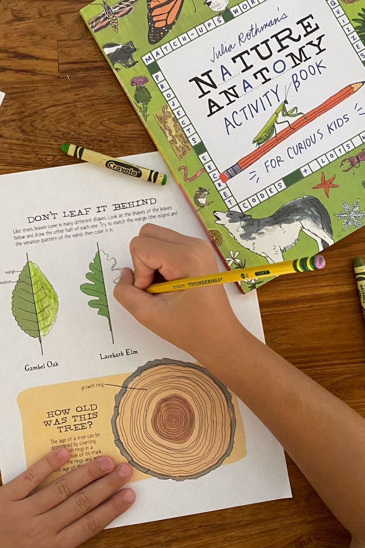 a child's hands holding a pencil and writing on paper next to an activity book