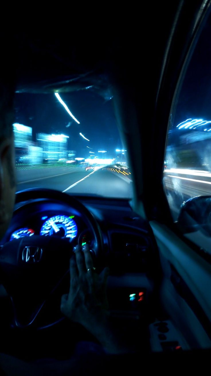 a man is driving his car at night with the lights on and blurry in the background