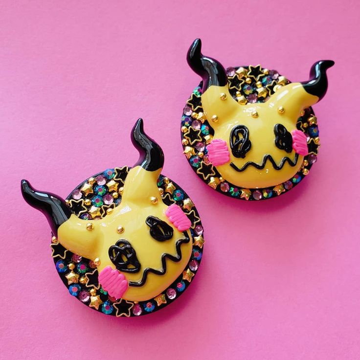 two yellow and black devilish hair clips on a pink background