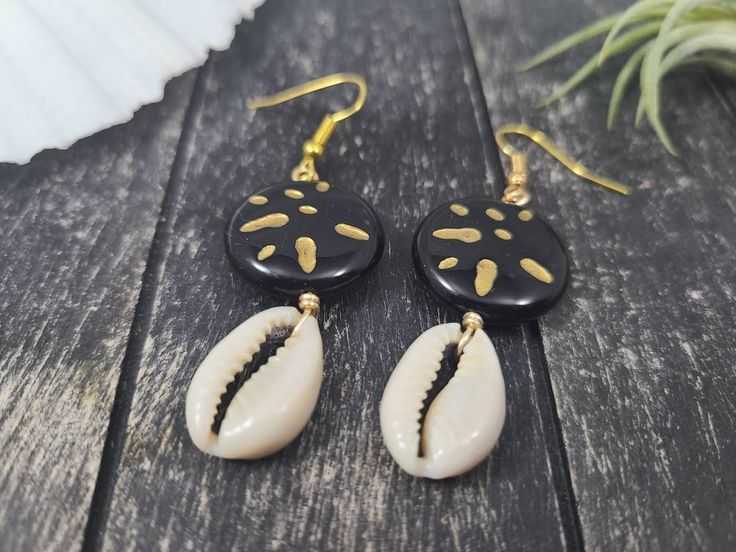 "These gorgeous dangle earrings feature genuine off-white sliced moneta cowrie shells dangling beneath 20mm round carved black and gold acrylic beads an etched Afrocentric abstract pattern. Aching for acrylics? Check out the rest of my acrylic jewelry here: https://etsy.me/2IadiWZ Throughout Africa and the Americas, cowrie shells have historically been viewed as symbols of womanhood, fertility, and prosperity. Check out my other cowrie shell jewelry here: https://etsy.me/2VQS0r0 These earrings m Cowrie Shell Earrings For Gifts, Black Shell Bohemian Jewelry, Handmade Black Shell-shaped Jewelry, Black Shell Jewelry For Gifts, Handmade Black Shell Jewelry, Black Shell Jewelry Gift, Black Shell Jewelry As A Gift, Bohemian Black Shell Jewelry, Artisan Black Jewelry For The Beach