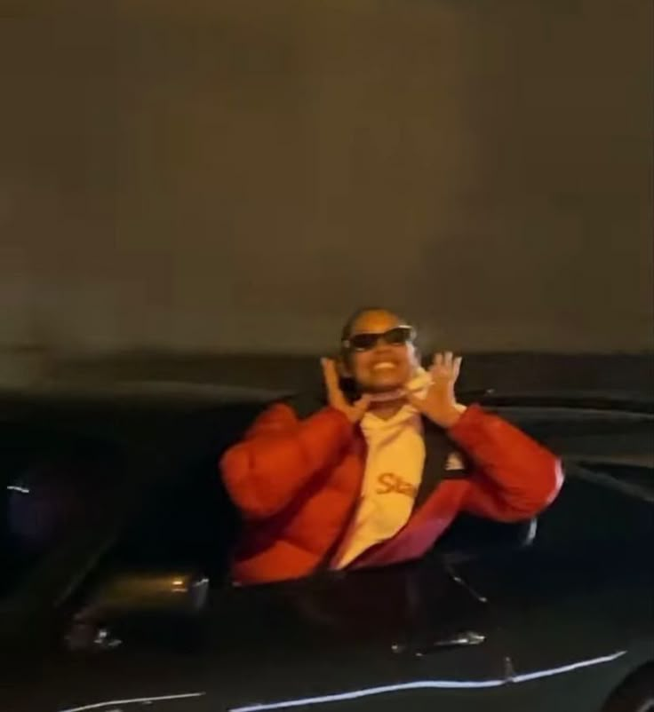 a man in an orange jacket and sunglasses sitting on top of a car