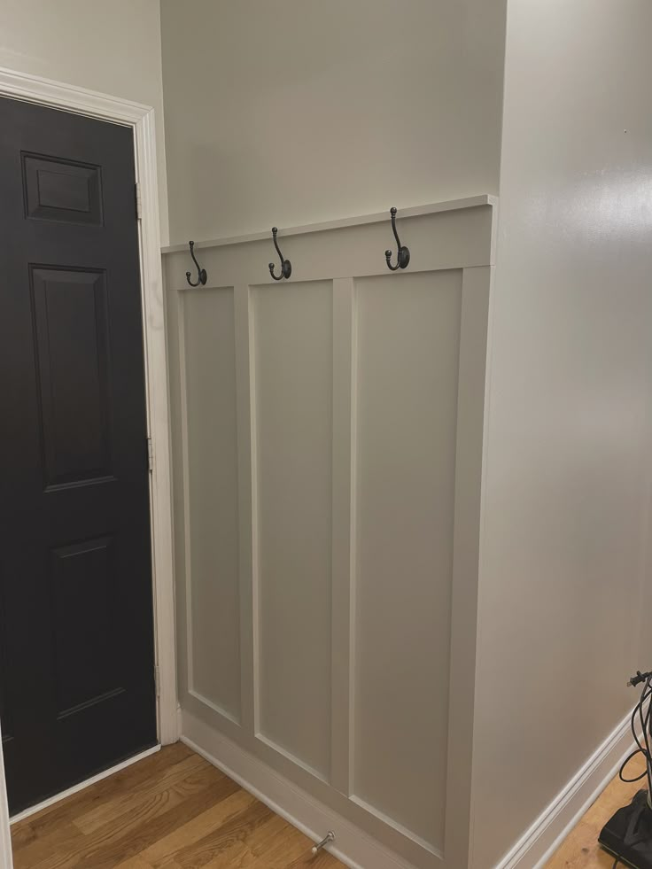 an empty room with two coat hooks on the wall and a black door in the background