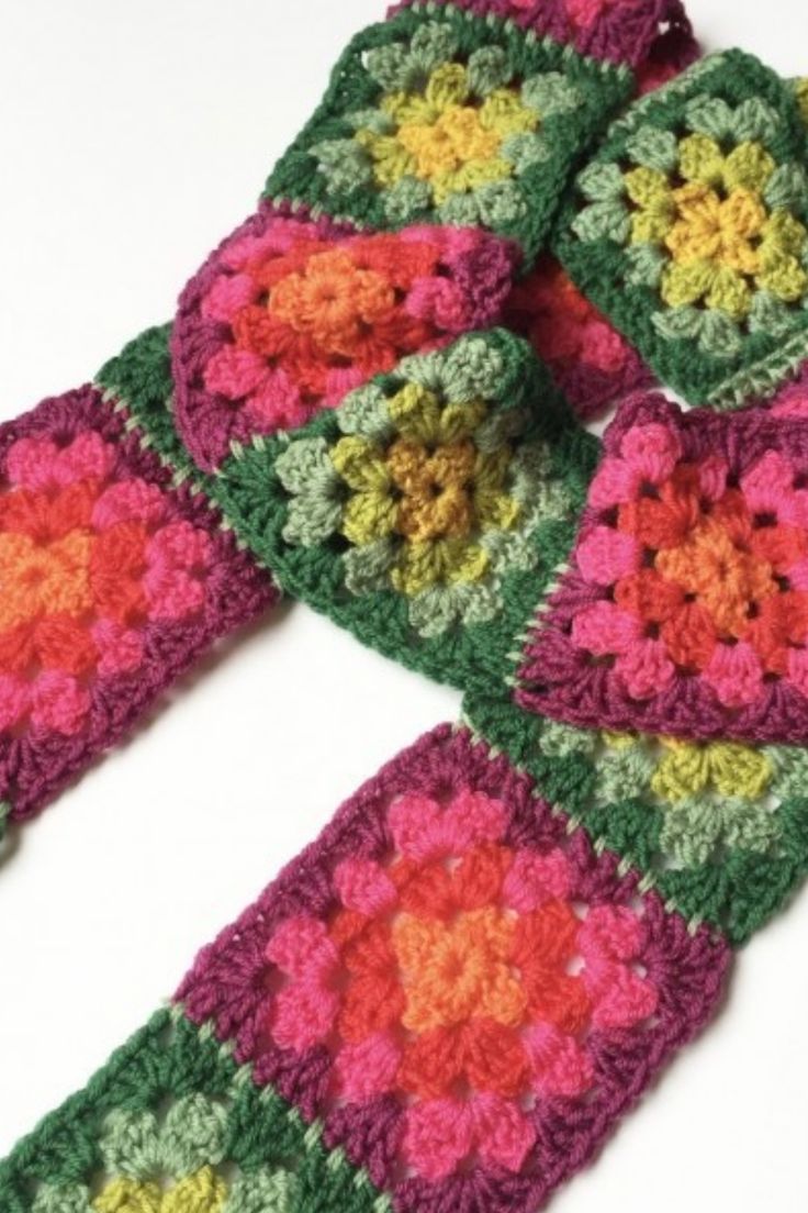 four crocheted squares are arranged in the shape of flowers on a white surface