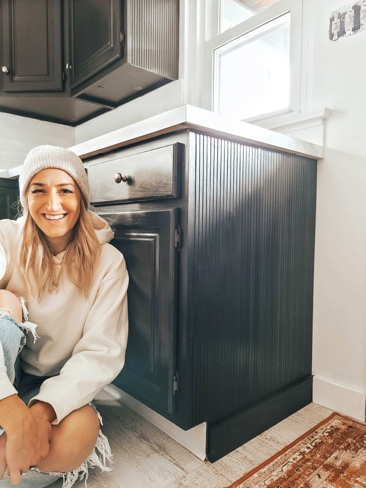 a woman sitting on the floor in front of an oven with her legs crossed and smiling