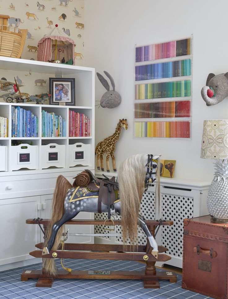 the toy horse is sitting in front of the bookshelf and toys on the floor