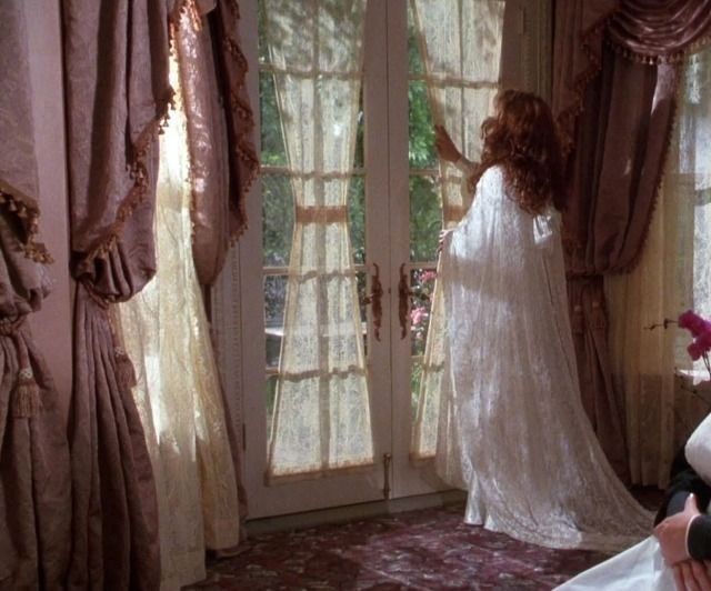 a woman in a white gown standing next to a window