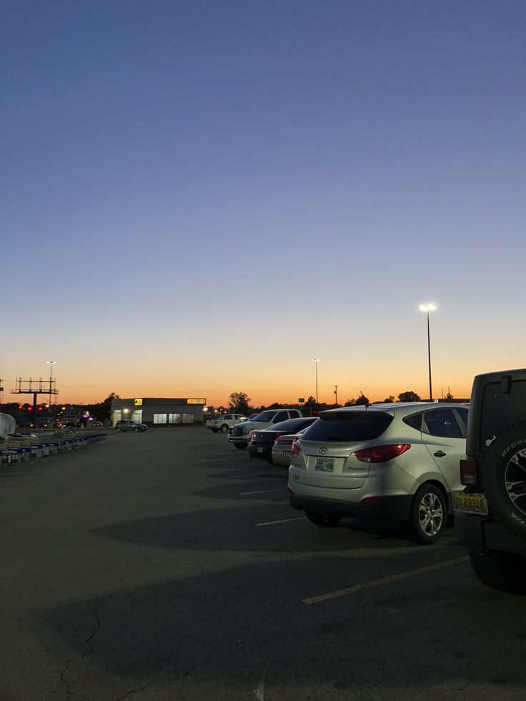 a parking lot filled with lots of parked cars under a blue sky at sunset or dawn