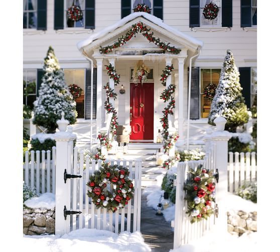 a white house decorated for christmas with wreaths on the front door and red door