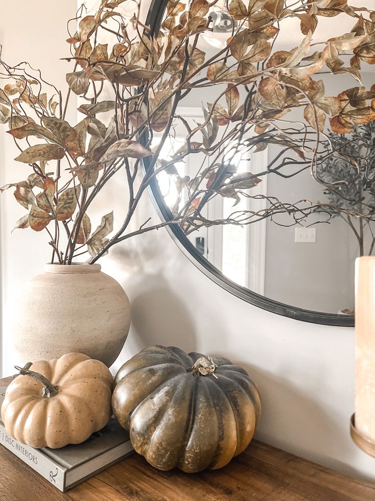 three pumpkins are sitting on a table in front of a round mirror and some branches