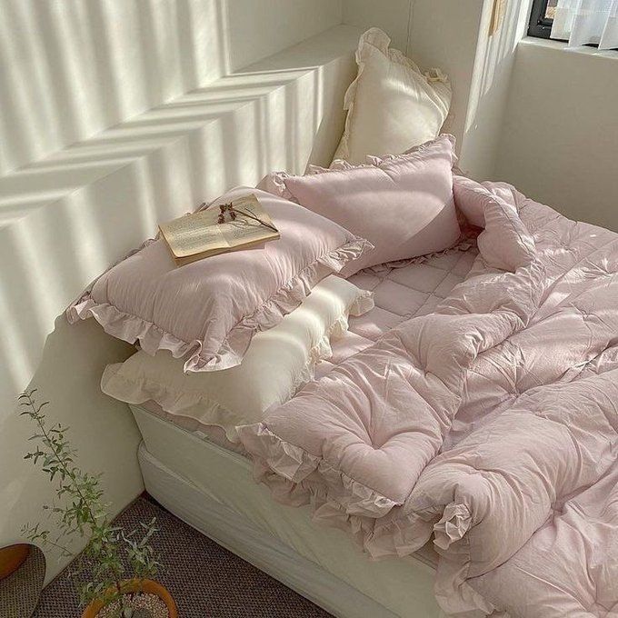 an unmade bed with pink comforter and pillows on it next to a potted plant