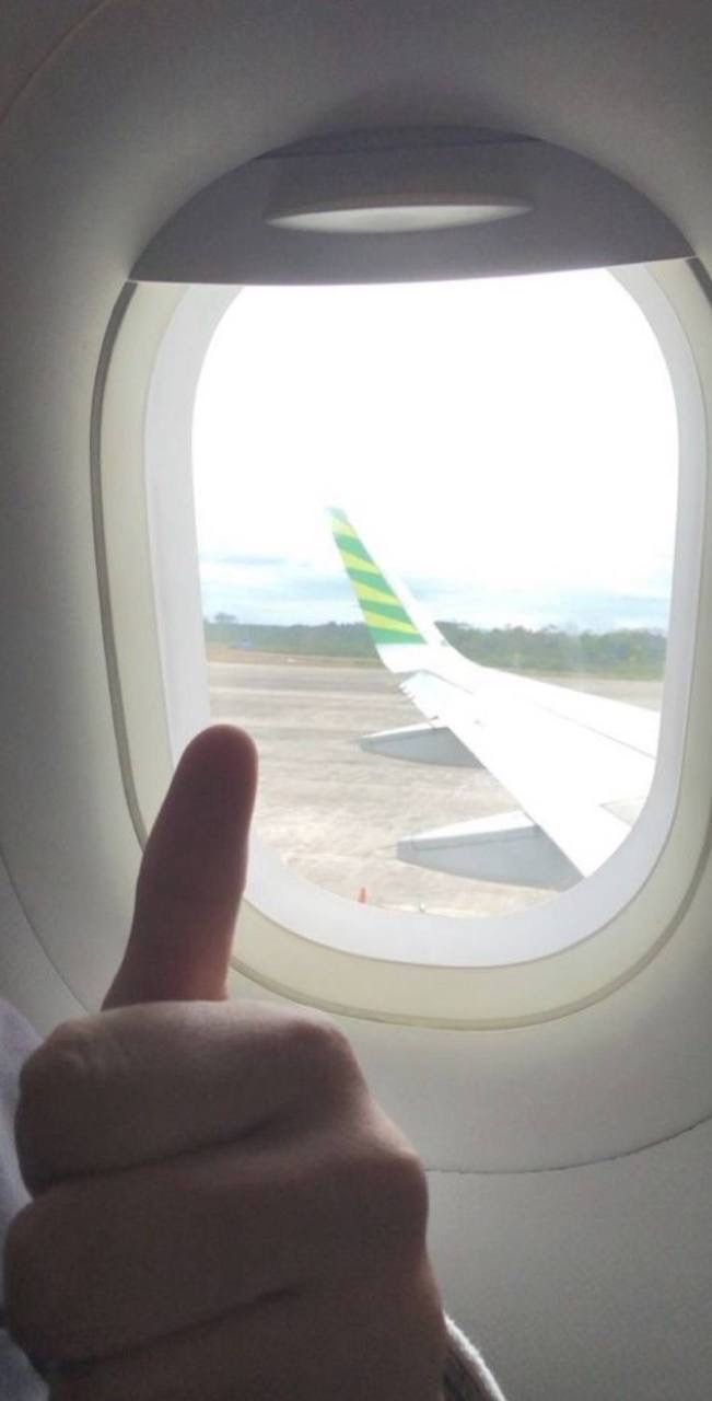 a person is giving the thumbs up sign in front of an airplane window that looks out onto the tarmac