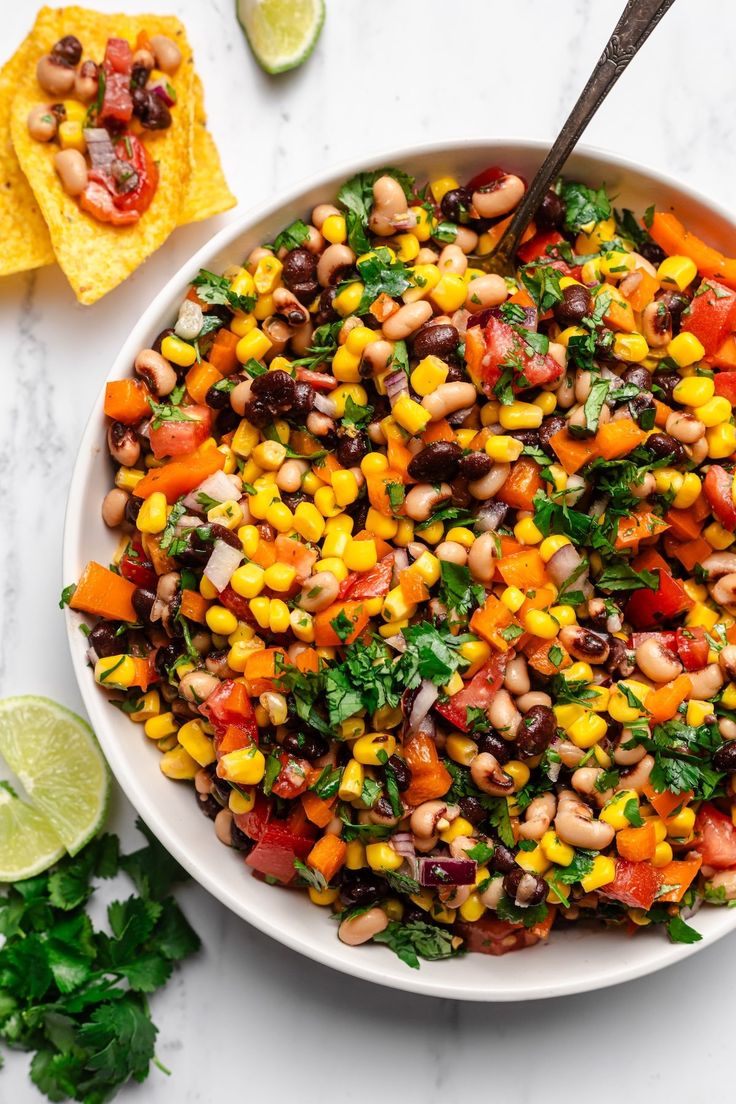 a white bowl filled with black eyed peas, corn, and cilantro next to tortilla chips