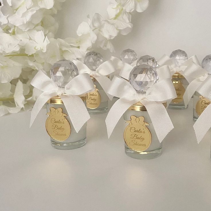 four small glass jars with white bows on them and some flowers in the back ground