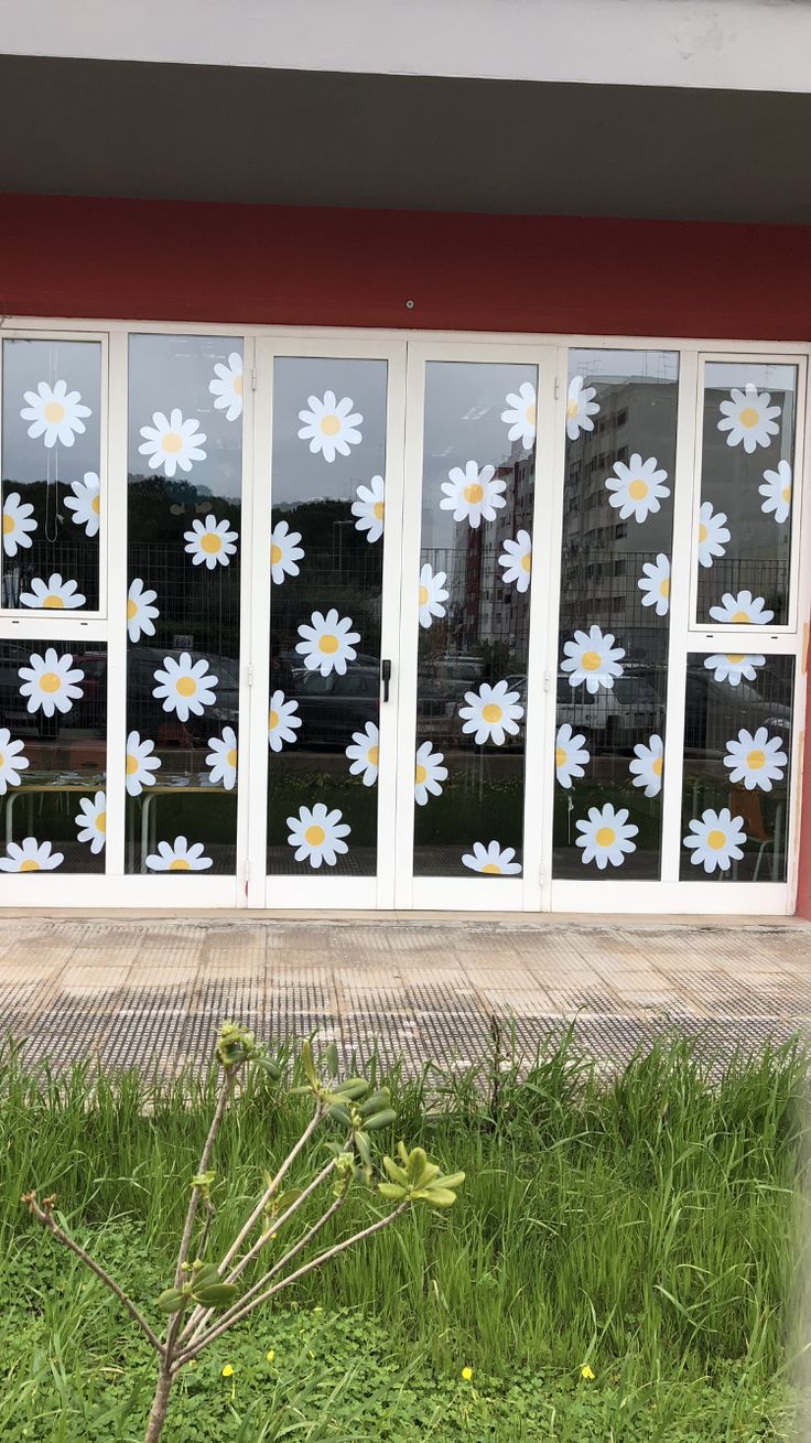 the window is decorated with white daisies in front of a red wall and green grass