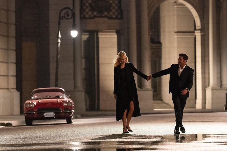 a man and woman holding hands while walking down the street in front of a car