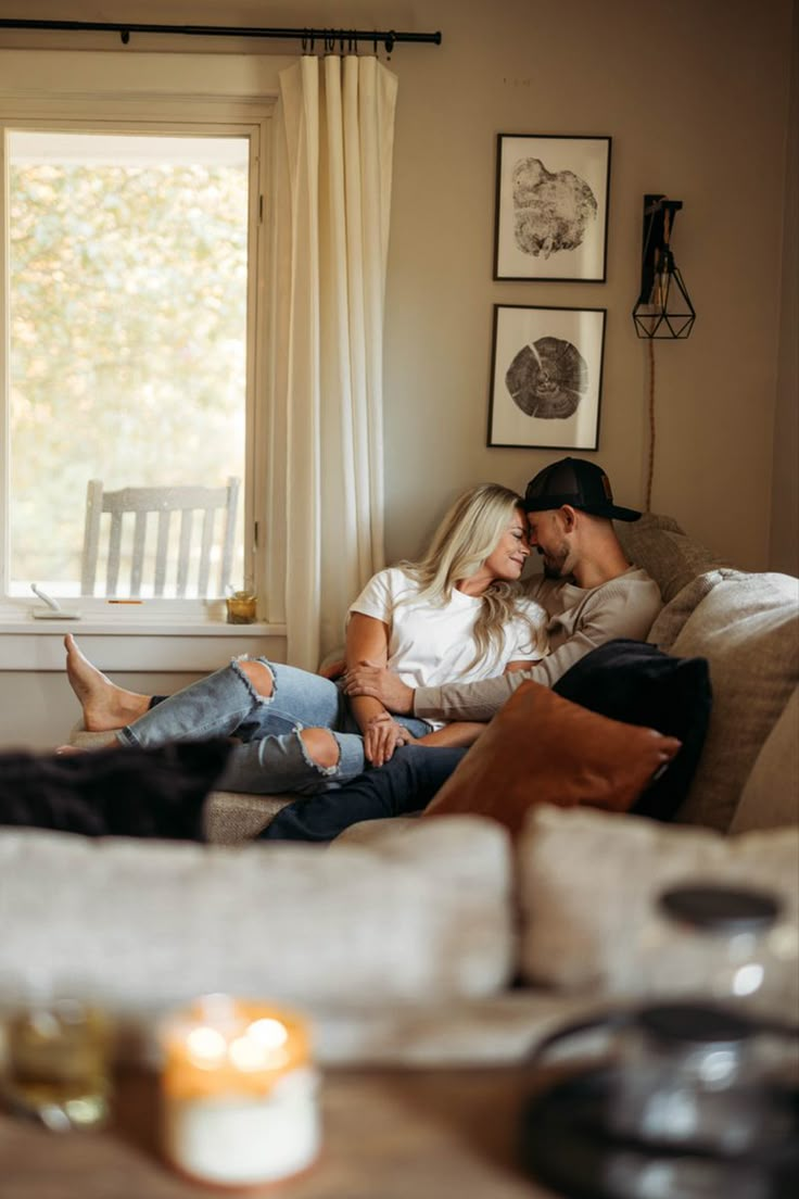 a man and woman sitting on a couch in front of a window looking at each other