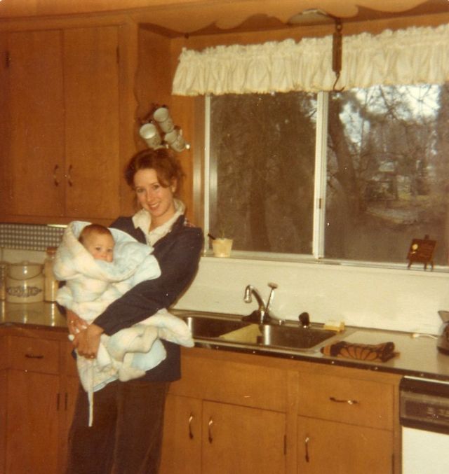 a woman holding a baby in her arms while standing next to a stove top oven