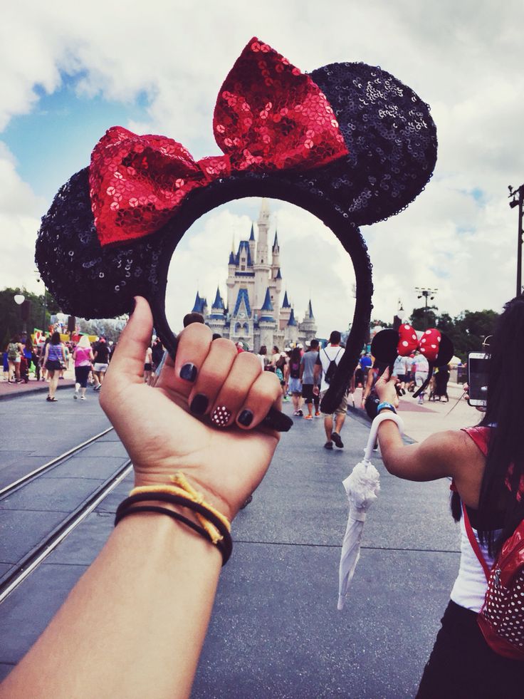 a person holding up a minnie mouse ears in front of a castle