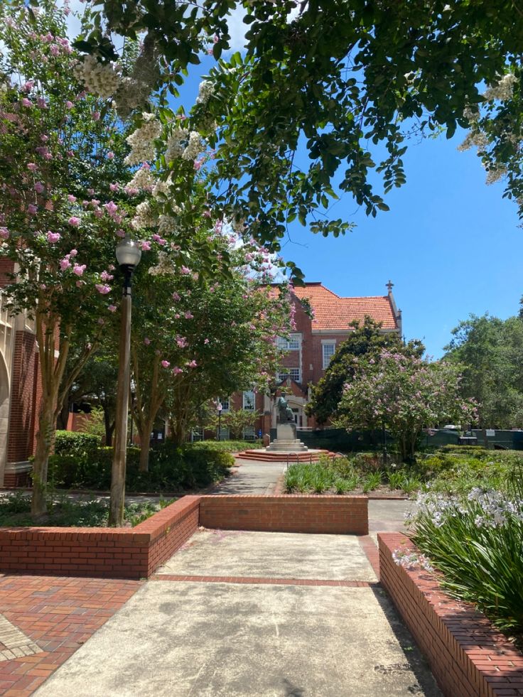 an empty walkway in front of a brick building with lots of trees and flowers on either side