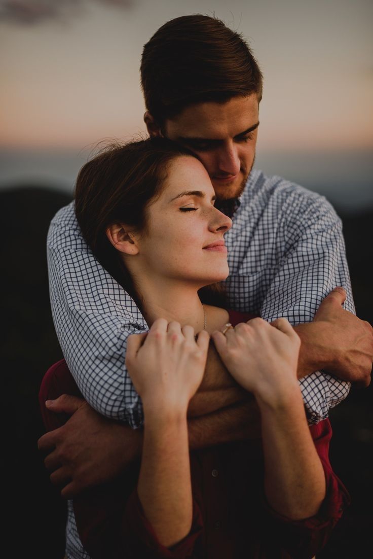 a man and woman embracing each other while the sun is setting