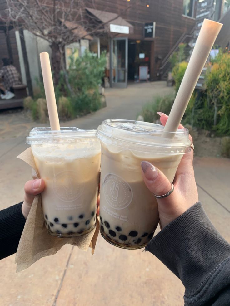 two people holding up drinks with straws in their hands on a sidewalk near a building