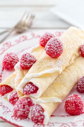 crepes with powdered sugar and raspberries sit on a red and white plate