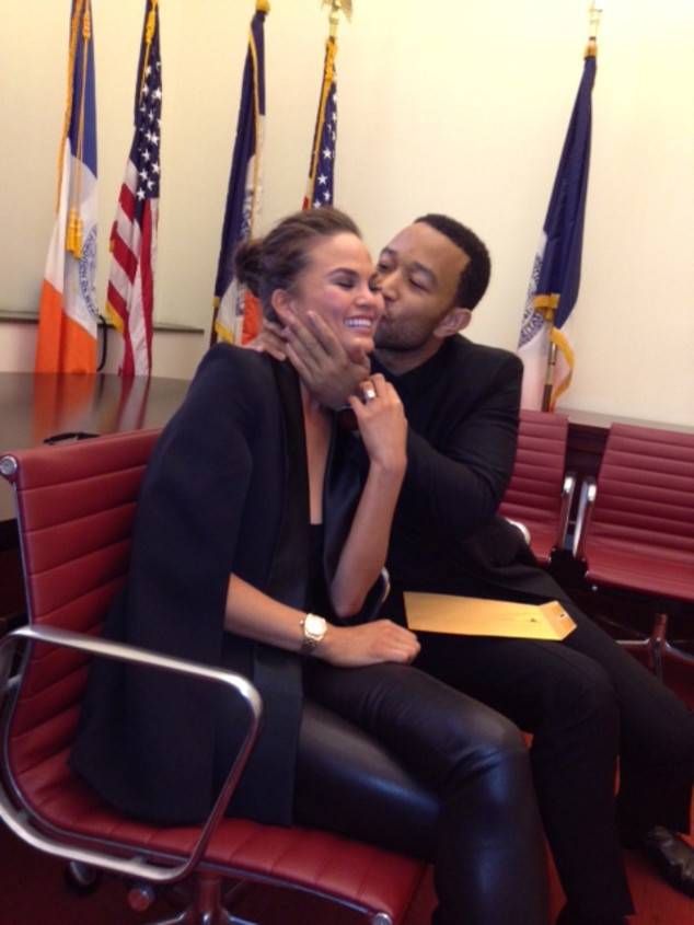 a man and woman sitting on a red chair in front of american flags with their faces close to each other