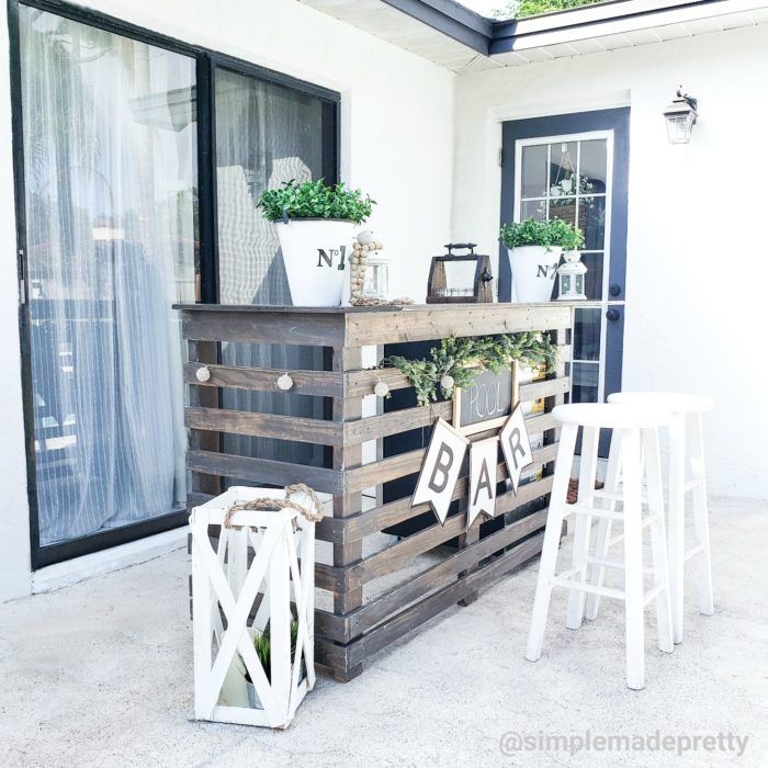 an outdoor bar made out of pallets with plants on top and two white stools