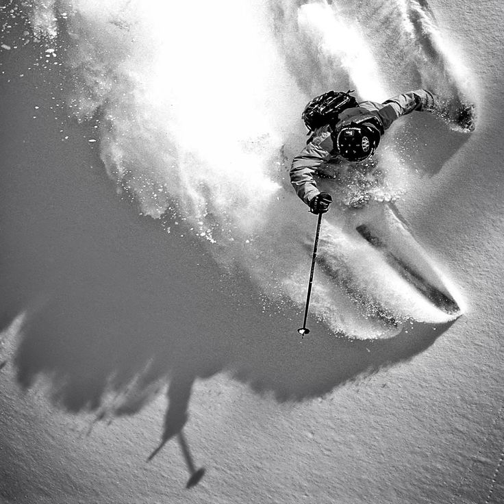 a man riding skis down the side of a snow covered slope with powder behind him