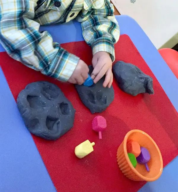 a young boy playing with play dough and toys on a red tableclothed surface