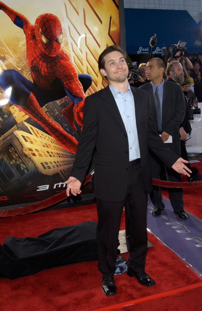 a man in a suit and tie standing on a red carpet at the spiderman premiere