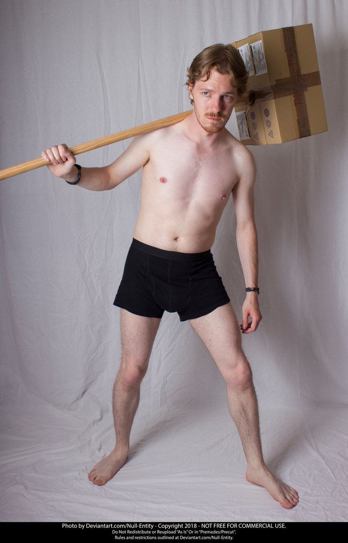 a shirtless man holding a wooden stick and cardboard box on his head while standing in front of a white backdrop