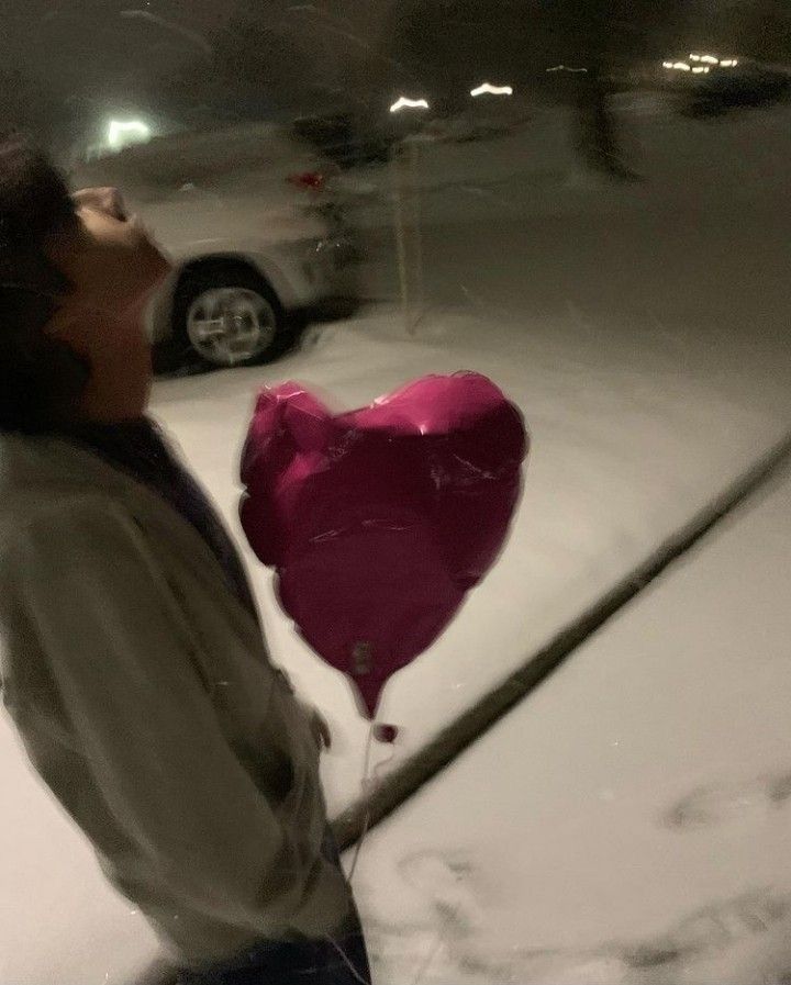 a man holding a heart shaped balloon in the snow