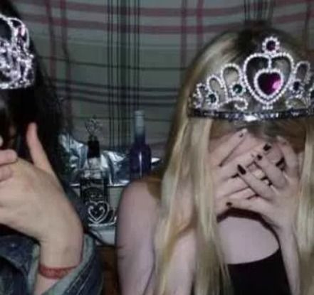 two women wearing tiaras and holding their hands up to their faces while looking at the camera