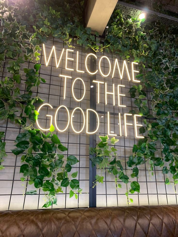 a sign that says welcome to the good life in front of a wall covered with plants