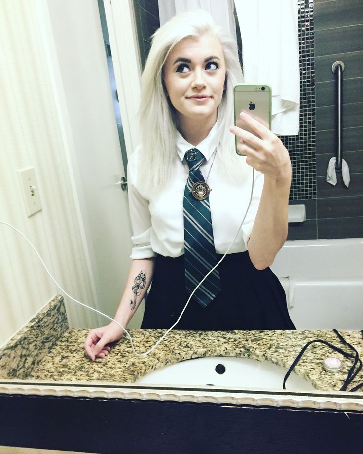 a woman taking a selfie in front of a bathroom mirror wearing a tie and headphones