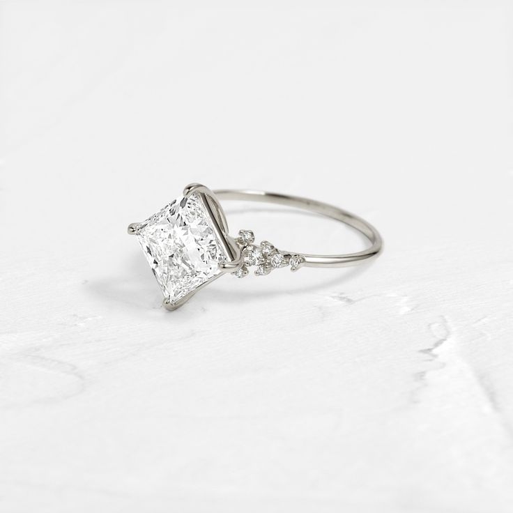 an engagement ring with a princess cut diamond in the center and three small diamonds on each side