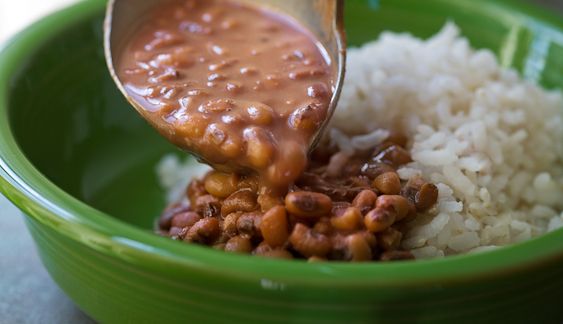 a green bowl filled with rice, beans and gravy being poured into it