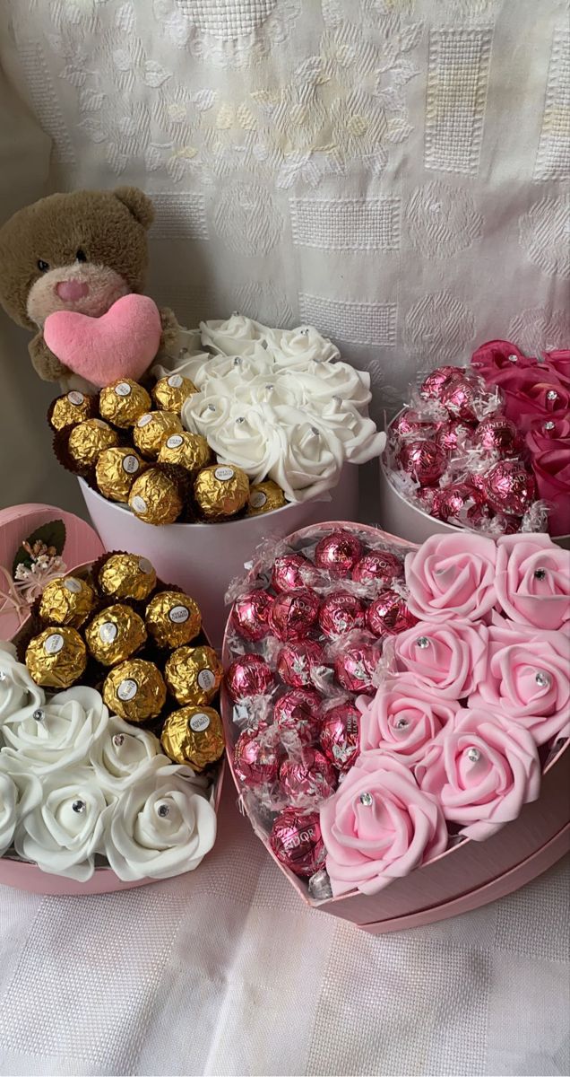 two heart shaped boxes filled with chocolates and roses next to a teddy bear on a bed